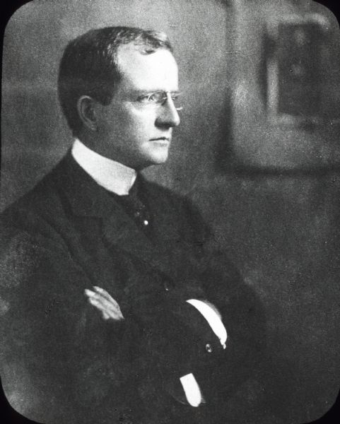 Studio portrait of James Deering (1859-1925) standing with his arms crossed. He is wearing eyeglasses and looking away from the camera.