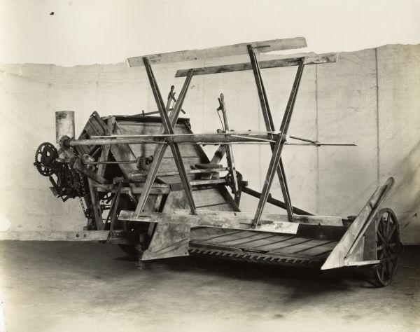 Side view of an early model grain binder in front of a backdrop.