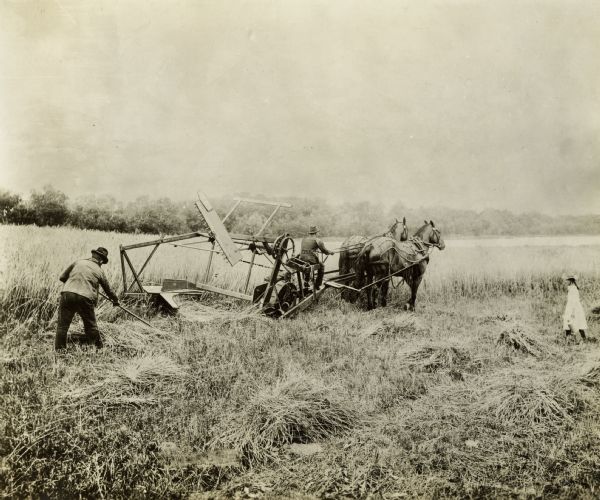 Two men are using a McCormick automatic self-rake to perform work in a field. A girl in a white dress and hat is standing to the side, wearing a dress and hat and holding what appears to be a milk pail. A handwritten caption on the photograph reads: "Reaper of 1858."
