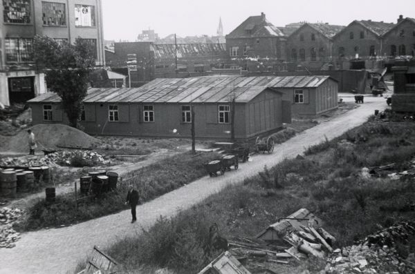 Elevated view of a man walking down a path surrounded by buildings, possibly damaged in World War II, at International Harvester's Neuss Works in Germany. The original caption reads: "Quarters built by Mr. Schneider to house offices in order to free buildings for manufacture; Neuss."