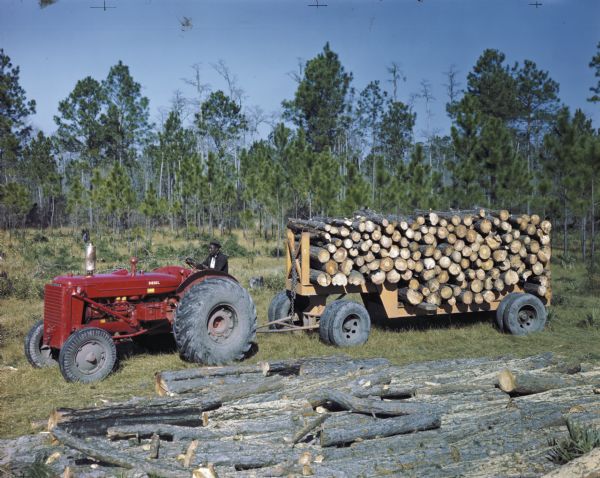 View of a man using a specially outfitted diesel tractor to haul a trailer loaded with cut logs. The original caption reads: "Two specially fitted tractors, an ID-9 and an I-4 are shown at work on a pulpwood project near Nahunta, Ga. for the Brunswick Pulp and Paper Co."