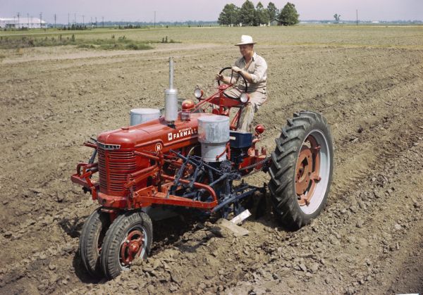 Slightly elevated view of a man using a McCormick Farmall H tractor with a forward cotton planter to work in a field. The original caption reads: "'Blackland' planting with HM-277 planter equipped with single-speed cotton hopper."