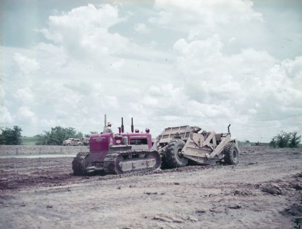 A man is operating a TD-14A crawler tractor (TracTracTor) with a BE Dozer used to form a reservoir. The original caption reads: "TD-14A owned by Manhattan Construction Co., Muskogee, Okla. Used with BE Dozer - dressing slopes for reservoir."