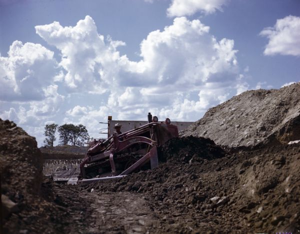 A man using a TD-14A crawler tractor (TracTracTor) with BE Dozer to excavate a reservoir. The original caption reads: "TD-14A owned by Manhattan Construction Co., Muskogee, Okla. Used with BE Dozer - dressing slopes for reservoir."