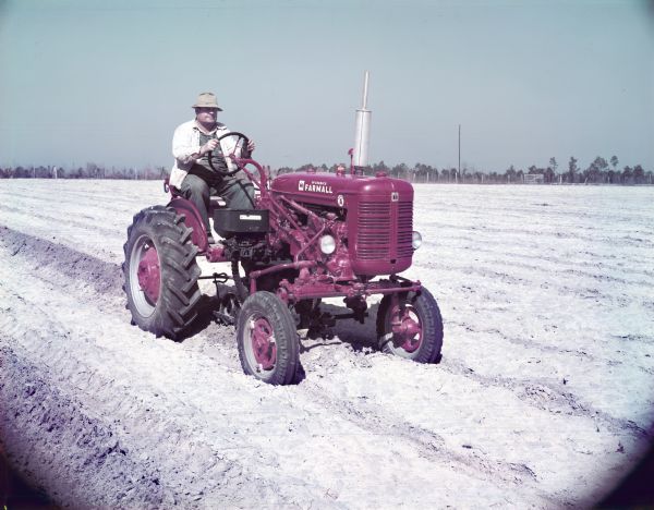 View towards a man, J.L. Aldrige, using a McCormick Farmall Super A tractor with a A-178 planter to work in a field. The original caption reads: "J.L. Aldridge of Waycross, Ga. planting corn with Farmall Super A and A-178 planter."