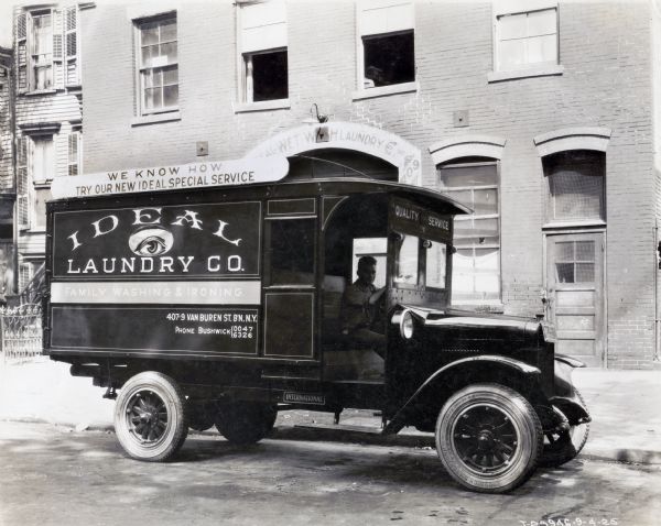 A man sits behind the wheel of an International truck used by the Ideal Laundry Company. In the background is a building with a sign over the door that says in part "Wet WH Laundry Co. Inc." The lettering on the truck reads: "We Know How / Try Our New Ideal Special Service; Ideal Laundry Co., Family Washing & Ironing; 407-9 Van Buren St. B'N. N.Y."