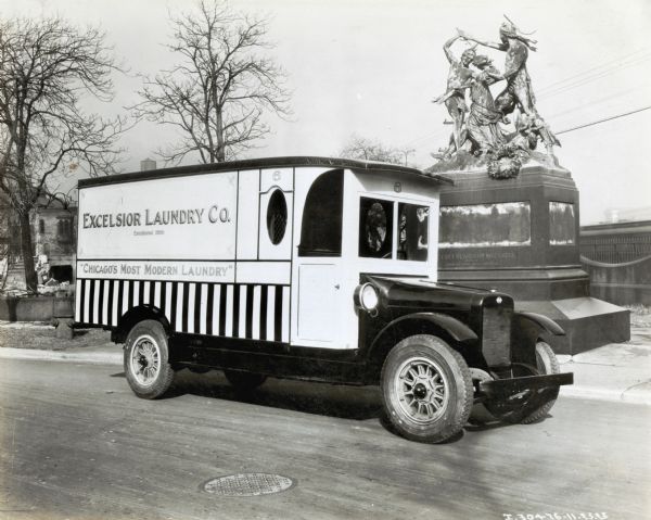 An International truck used by the Excelsior Laundry Company is parked along a street in front of a monument for the Fort Dearborn massacre. The lettering on the truck reads: "Excelsior Laundry Co., Established 1890; Chicago's Most Modern Laundry."  The monument reads: "...Fort Dearborn Massacre, August 15, 1812; Black Partridge Saving Mrs. Helm."  The monument was erected in 1893 and originally stood at the intersection of 18th and Calumet Streets, the presumed location of the massacre.