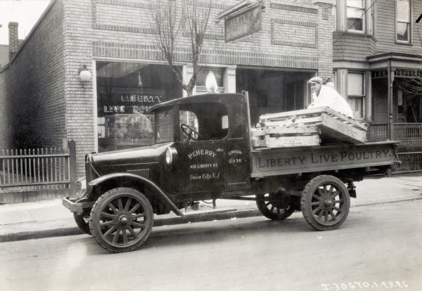A man loads pallets of chickens onto the back of an International truck in front of the Liberty Live Poultry storefront. The truck reads: "P. Cherry; 415 Liberty St., Union City, N.J."
