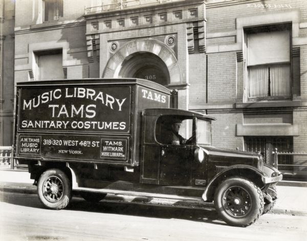 An International truck used by the Tams Music Library parks outside a large brick building with an arched entrance. Above the entrance is the address, "305". The lettering on the truck reads: "Music Library TAMS Sanitary Costumes; A.W. Tams Music Library, 318-320 West 46th St. New York; Tams Witmark Music Library Inc." Tams-Witmark Music Library, Inc. was incorporated in January 1925 as a result of the consolidation of the Arthur W. Tams Music Library and the Witmark Music Library.