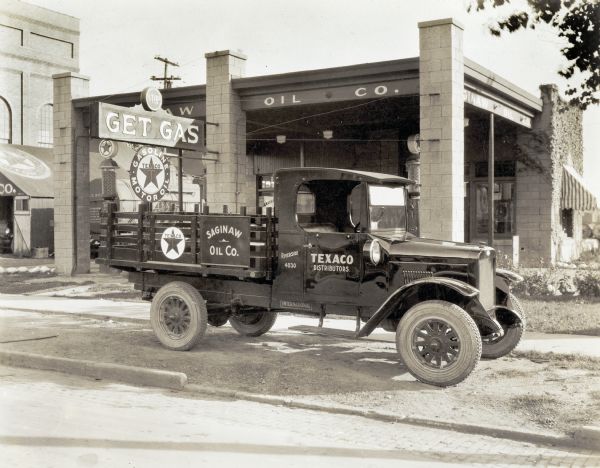An International truck used by the Saginaw Oil Company parked in front of a Texaco filling station.