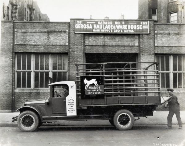 An International truck used by Ascher's 100% Pure Wool Knit Goods Company parked in front of a building marked: "Gerosa Haulage & Warehouse." One man is sitting in the cab, and another man is standing and holding onto the gate in the back of the truck. The sign on the building reads: "Main Office 280 E.137th St."