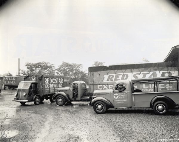 A group of International trucks used by the Red Star Express Lines Company parked in a gravel lot. Men are sitting in the cabs of the trucks. The lettering on the trucks reads: "City Delivery" and " Auburn, Syracuse, Rochester."
