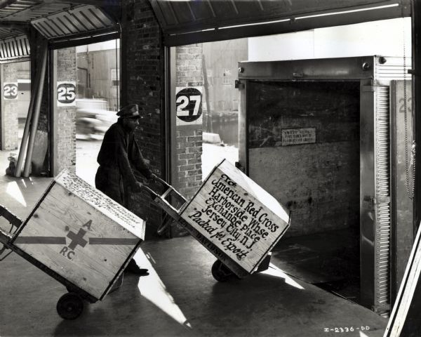 A worker at Davidson Transfer & Storage Company's loading dock moving a wooden crate marked "American Red Cross" onto the back of a waiting truck (possibly an International D-40).