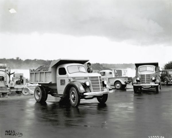 A group of road repair trucks are parked in a paved parking lot at Niagara Falls, Ontario, Canada. A man is standing near one of the trucks. The original caption reads: "Road Repairs - 2 D40's, 134" w.b. - Brennan Paving Co., D-2 Pickup also."  The photograph was taken in Niagara Falls, Ontario, Canada.