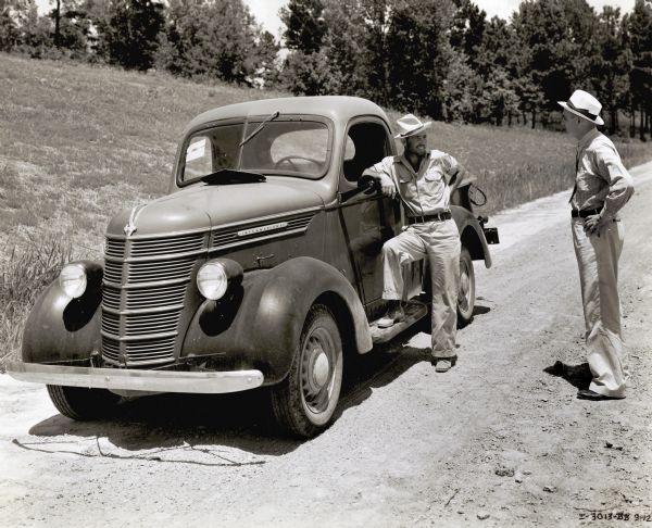 Charles Thomas, manager of the Jackson, Mississippi International Harvester dealership, leans against an International truck while speaking with Robert D. Downey, superintendent of the Hodgins-Adams Company. The men are standing on the Natchez Trace Parkway during the process of its completion.