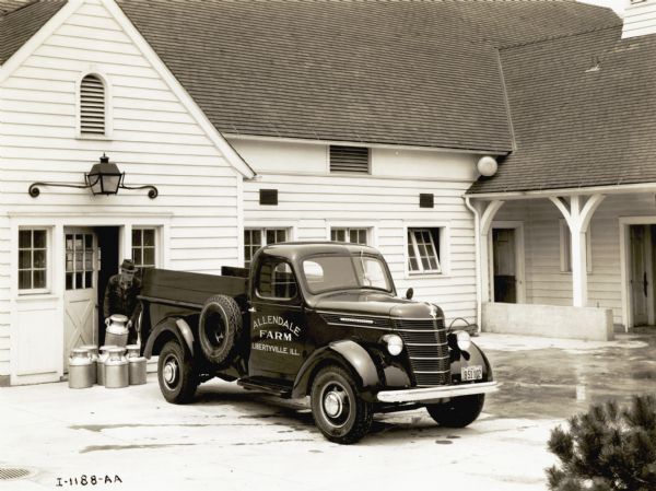 A man near the open door of a farm building loads milk pails into the back of an International D-15 pickup truck used by the Allendale Farm.