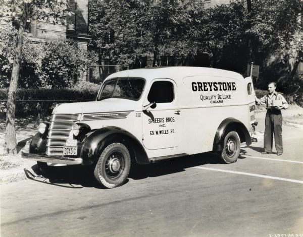 A man opens the rear door of an International truck used by Spheeris Brothers Inc. The original caption reads: "Model D2, 125" W.B. - 6.00 - 16 tires." The text on the truck reads: "Greystone Quality DeLuxe Cigars" and "Spheeris Bros. Inc., 531 W. Wells St." Spheeris Brothers Merchandising was a wholesale tobacco business.