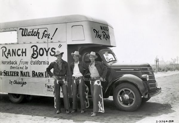 The "Ranch Boys." Three men wearing rodeo gear and cowboy hats, pose by the passenger door of an International D-30 truck outfitted with a trailer. The original caption reads: "A Model D-30 motor truck owned by Jack Ross of the Ranch Boys, who are riding horseback from Los Angeles to New York City using the truck to haul three relief horses.  The picture shows Joe Bradley, Jack Ross, and Shorty Carson, members of the Ranch Boys trio." The text on the trailer reads: "Watch for! ...Ranch Boys. Horseback from California, Overland to...a-seltzer Nat'l Barn...in Chicago."
