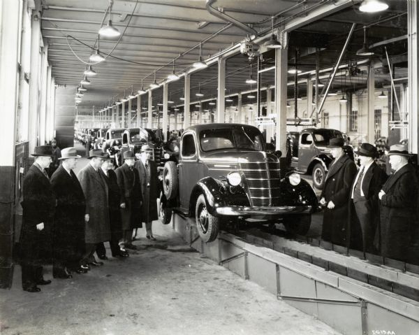 A group of men wearing overcoats and hats are standing on either side of an International truck on the assembly line at International Harvester's Springfield Works (factory).