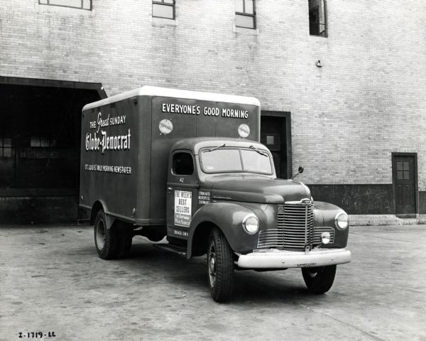 An International truck used by the Globe-Democrat newspaper is parked in front of what appears to be the loading dock of a brick building. The text on the truck reads, "The Great Sunday Globe-Democrat," "St. Louis' Only Morning Newspaper," "Everyone's Good Morning," and "The Week's Best Sellers."
