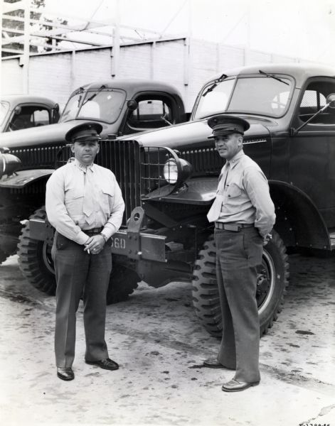 Two uniformed Marines stand in front of International trucks parked in a row. One man holds a cigarette in his hands. The original caption reads: "Captain George C. Carroll, motor transport officer. Second U.S. Marine Division; right: Major James M. Ranck, motor transport officer, Marine Corps base, San Diego. Trucks in background are 1 1/2-ton 4-wheel-drive Model M-3-4 with standard cab and cargo body."