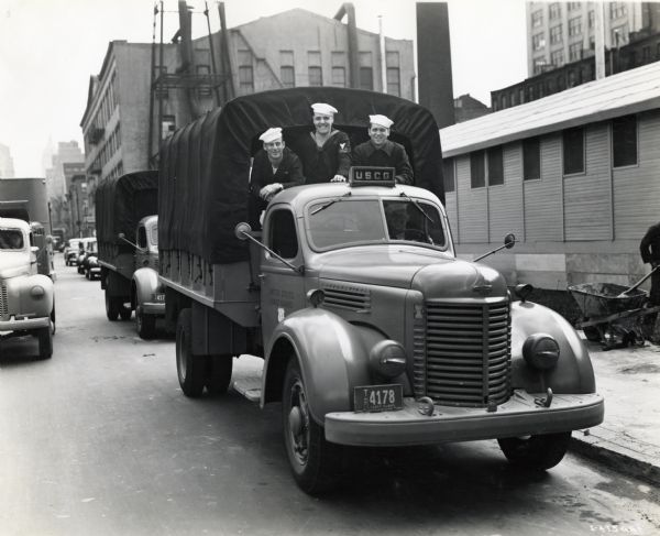 Three men of the United States Coast Guard ride in the back of an International truck. The photograph was probably taken in front of Camp Chelsea. The original caption reads: "In the accompanying illustrations is shown a fleet of International K-5 & K-6 cargo trucks in convoy formation used to transport United States Coast Guard seamen with their gear to Camp Smith. In another illustration, a close-up of one of these cargo trucks is shown in front of Camp Chelsea in the heart of New York City, where men of the New York Port Security force are quartered."