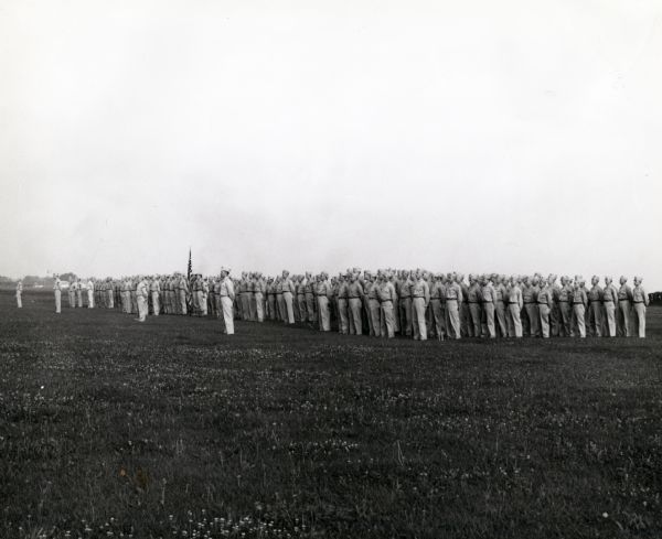 A group of soldiers lined up in a field for a Saturday morning review  and a parade before officers. The soldiers likely belong to the "Harvester Battalion" at Camp Perry, Ohio for training. The battalion was made up of former International Harvester employees and dealers.