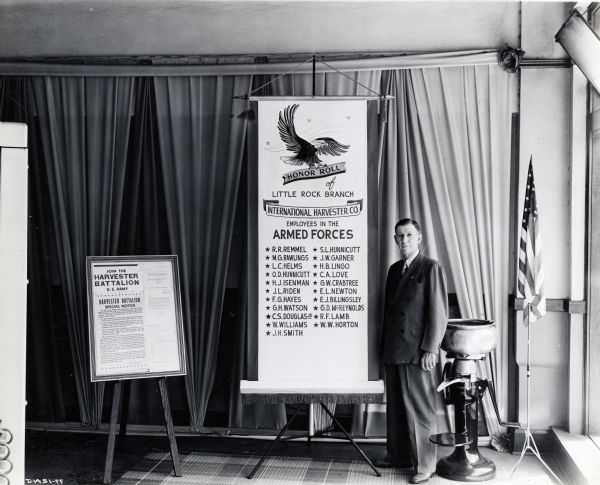 S.E. Foster, manager of International Harvester's Little Rock branch house, stands beside the branch honor roll of enlisted International Harvester men. Also included in the display is an American flag, a cream separator, and a framed notice to join the Harvester Battalion / U.S. Army.