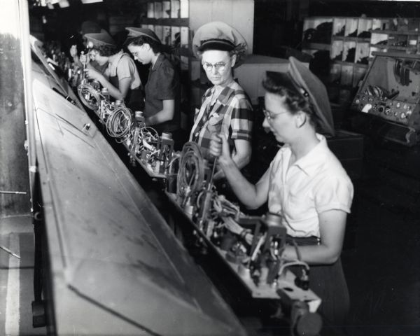 A line of female factory workers at International Harvester's Bettendorf Works assembling the instrument panels for "M-5 high speed tractors" [crawler].