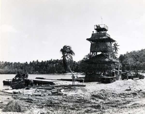 Men of the 34th Construction Battalion of Seabees work around a boat dock using an International TD-9 TracTracTor (crawler tractor) at Halavo Seaplane Base. A palm-covered operations tower is to the right of the dock. Halavo Seaplane Base was located at Halavo Bay, Florida Island, Solomon Islands. The original caption reads: "K-8 truck at extreme right."