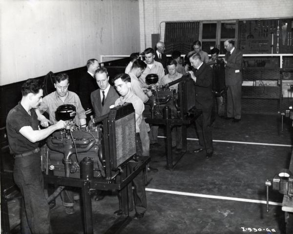 Fowler McCormick and other International Harvester executives look on as men stand at stations with truck engines at the U.S. Navy Motor Vehicle Maintenance School.