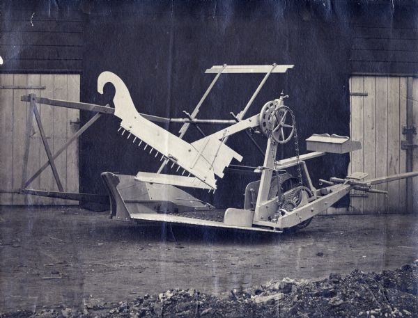 McCormick self-delivery [self-rake] reaper with buildings in the background. The reaper appears to be the model that Cyrus McCormick displayed at the London Exhibition of 1862.