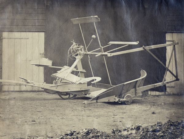 McCormick Self-Delivery [self-rake] reaper parked in front of some wooden buildings. The reaper was likely the model displayed by Cyrus McCormick at the London Exhibition of 1862. A handwritten caption with the photograph reads: "McCormick reaper as used in the harvest of 1862."