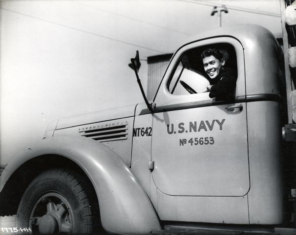 Close-up of C.D. Yoakum, M.M. 3/c, driver of an International K-7 truck used by the United States Navy. The original caption reads: "A number of standard K-7 Internationals with stake bodies are utilized at the Port of Hueneme for general hauling. Some of them are provided with seats as shown and serve as personnel carriers. At night these K-7's are parked in a group with other standard International models, as shown in photo I-1776-HH."