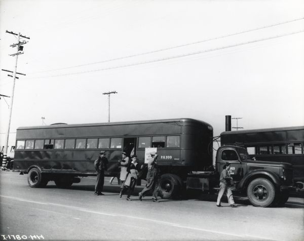A group of civilian workers from Port Hueneme exit an International trailer used in transportation to and from the naval base. The original caption reads: "In the transport of the thousands of civilian employes [sic] to and from the Port of Hueneme, International tractor-trucks, pulling huge bus-type trailers, are used as shown. The "single-shots" show a late Model KR-11 pulling a trailer bus, whose seating capacity is 72 passengers. The bus shown was bound for Santa Barbara, 45 miles away. It was making a round trip of 98 miles and 14 stops each way."