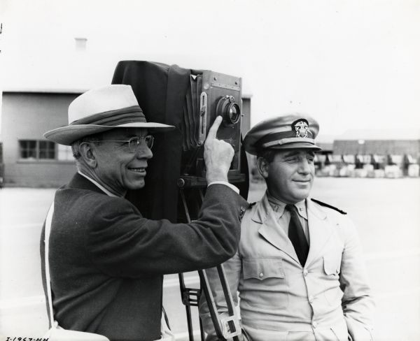 E.A. Hunger of the International Harvester Company adjusting a view camera on a tripod to take a photograph at the Port of Hueneme military base. P.P. Pasqualino, in charge of yard operations at the advanced depot, is standing beside him.