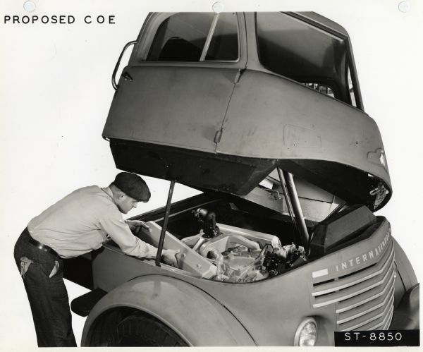 A man working on a truck engine in the opened compartment of an experimental "flip cab." The text in the upper left corner reads: "Proposed COE [cab-over-engine]."