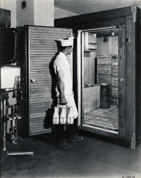 A man carrying milk bottles stands at the doorway to a walk-in cooler at the Eubanks Dairy.