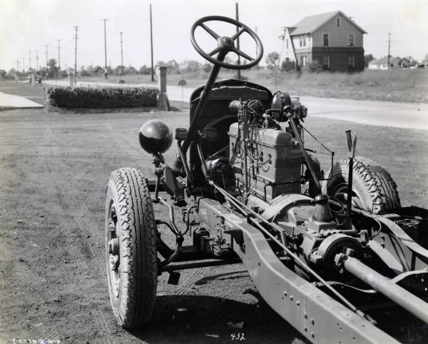 Exposed chassis and engine of an International C-35 or C-35 B truck looking toward the steering column. The vehicle is parked outdoors in a lot near a road, with houses in the background.