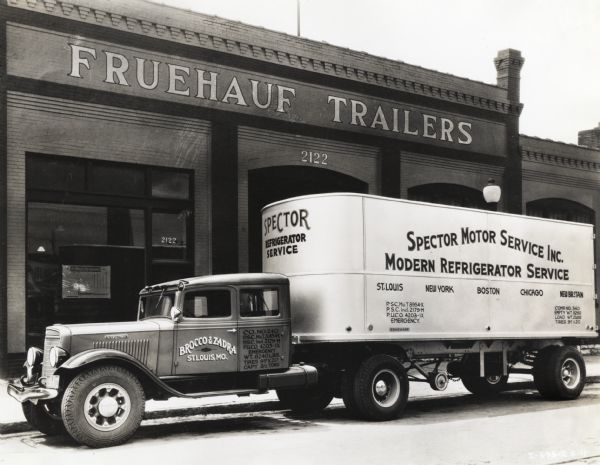 An International truck with a trailer used by Spector Motor Service Inc. parked in front of a Fruehauf Trailers storefront. The text on the truck cab reads: "Modern Refrigerator Service" and "Brocco & Zadra, St. Louis, MO."