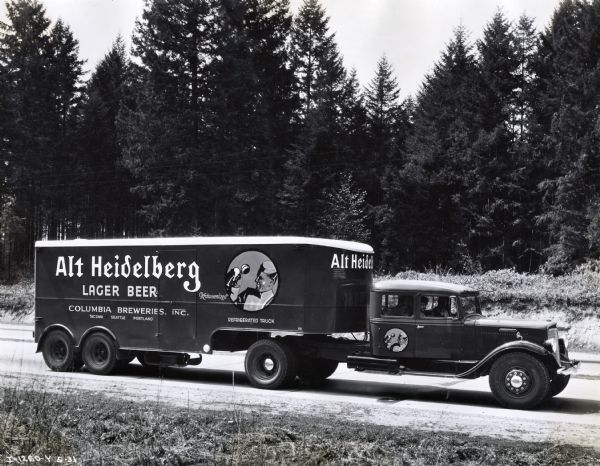 Two men sit in the cab of an International C-50 truck parked on a dirt road. The refrigerated truck was used by Columbia Breweries, Inc., of Tacoma, Washington and had a 14 ton capacity. The text on the side of the truck reads: "Alt Heidelberg Lager Beer; Columbia Breweries, Inc.; Tacoma, Seattle, Portland."