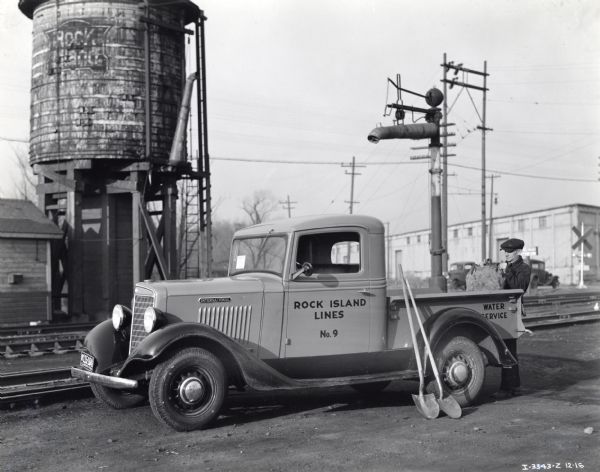 A man places a bag onto the bed of an International C-1 truck owned by the Chicago Rock Island Railroad. The truck is marked with the text "No.9" and "Water Service."