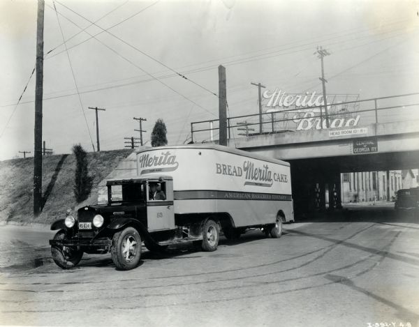 An International truck used by the American Bakeries Company parked alongside a road near an overpass. The text on the truck reads: "Merita Bread, Cake" and there is a billboard advertising "Merita Bread" in the background.
