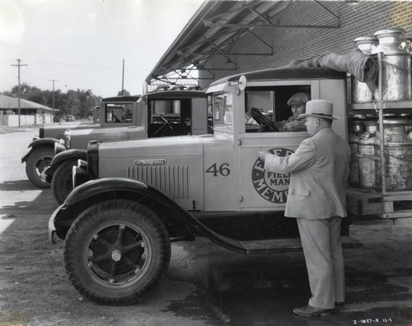 Men unload milk cans from International motor trucks at the Dairymen's Cooperative Creamery in Boise Valley. J.H. Brown, manager, stands beside the truck.