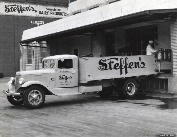 A man loads milk cans onto the back of an International truck used by Steffen's Ice Cream. Signs in the background read: "Steffen's Sunshine Dairy Products" and "Plant B."