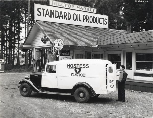 J.P. Whalen of the Continental Baking Company loads an International truck marked: "Hostess Cake" with boxes outside the Hilltop Market service station.