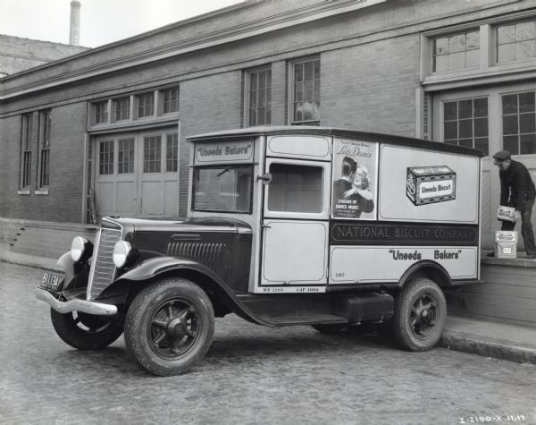 A man loads boxes marked "Sky Flake Biscuits" onto the bed of an International Model C-35 truck owned by the National Biscuit Company. Advertisements on the truck read: "Tune in 'Uneeda Bakers' Let's Dance," "3 Hours of Dance Music," "Uneeda Bakers," and "Uneeda Biscuit."