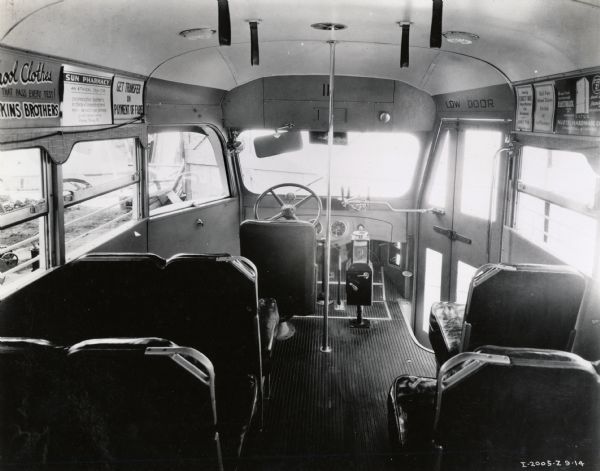 Interior of an International bus, looking toward the steering wheel. The bus appears to be part of a public transportation fleet with advertising signs hanging near the roof on either side of the aisle.