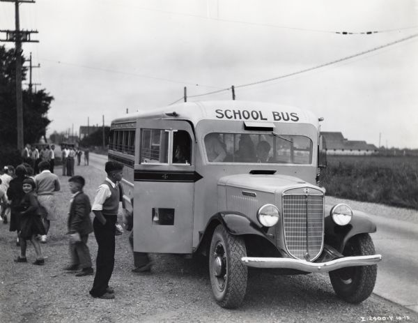 Children disembark a school bus parked along a road in a rural area.  The bus was owned by Fife, Washington schools, along with an A model, a C-40, and a C-60.