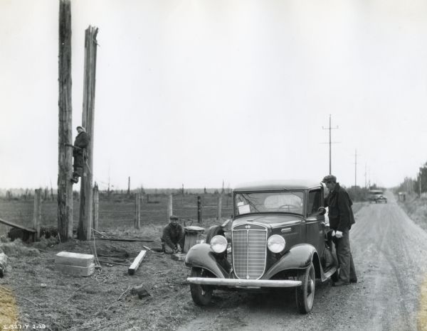 An International C-1 truck is parked along the side of a dirt road while men work on repairing damaged power poles. The original caption reads: "Nos. 109 and 110 photographs were made in the vicinity of Sumas, Washington, and show the C-1 just delivered to the Puget Sound Light and Power Company's branch in that territory. This unit was immediately pressed into service to assist in restoring light and power service that had been completely disrupted in the northern part of this state by one of the worst blizzards and silver thaws that had been experienced in many years."